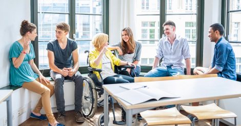 A képen egy fiatalokból álló társaság látható beszélgetés közben. Egy szőke hajú lány kerekesszékben ül.